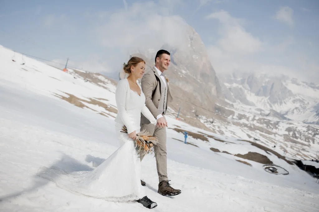 Newlywed couple walking on the snow on Seceda in the Dolomites after a civil wedding ceremony.