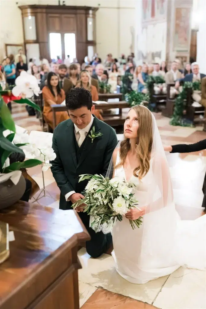 The bride and groom are kneeling in front of the statue of the Virgin Mary.